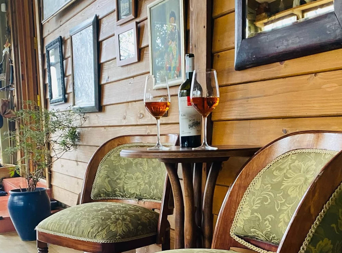Glasses of amber (orange) skin contact wine from Kisi varietal on table with chairs and Georgian art on wall in background