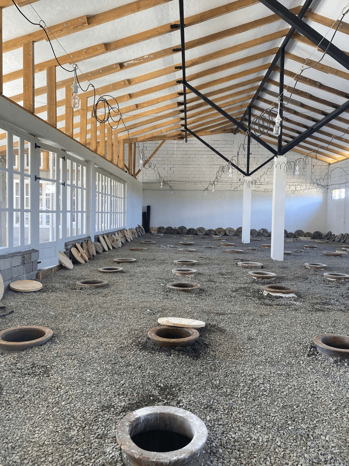 Anapea Village fermentation marani (wine celler in Georgian) with empty Qvevi ready for harvest and wine fermentation in large building. Lids for the qvevri once fermentation starts are stacked along the walls