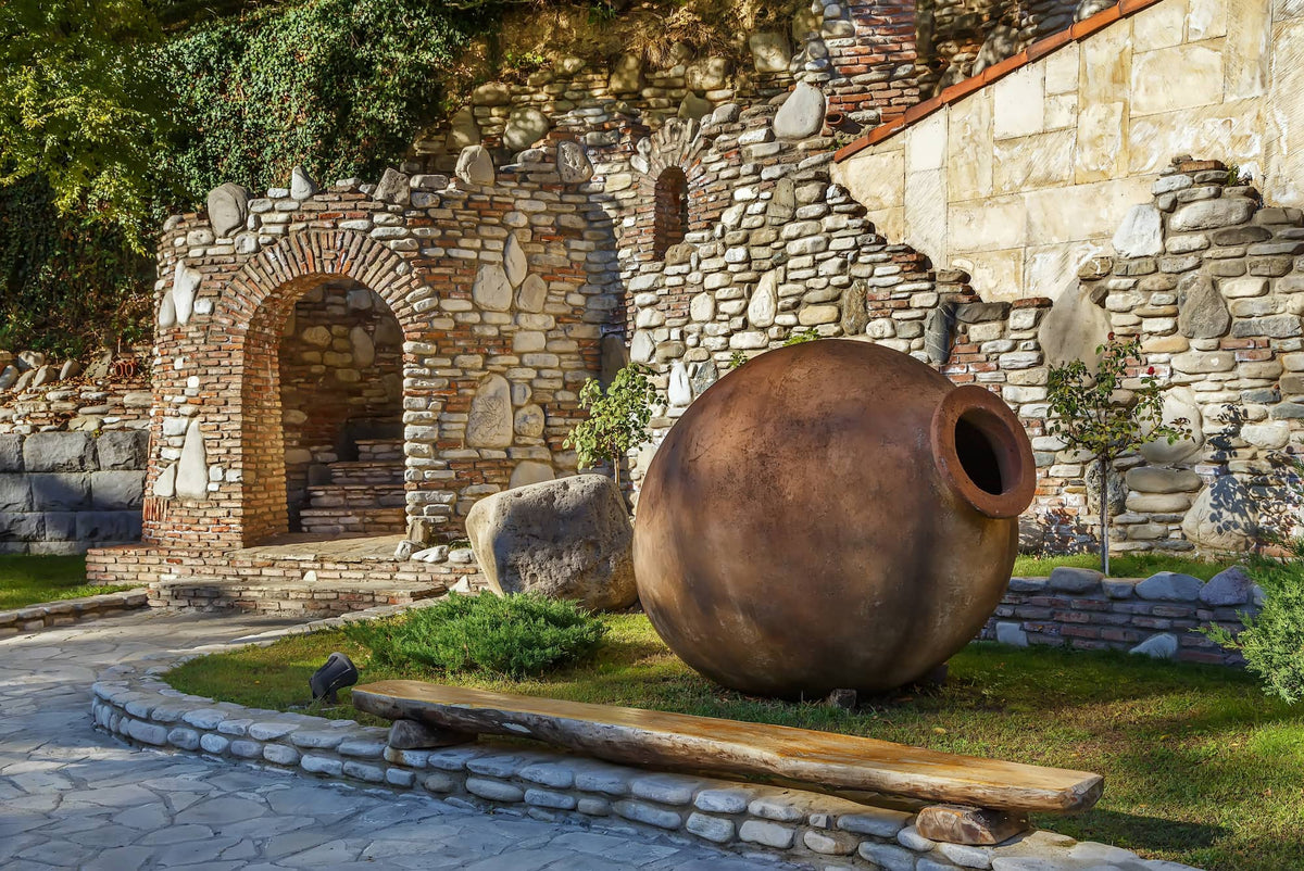 Large Qvevri on it's side above ground with amazing ancient stonework and archway to stairs surrounding it
