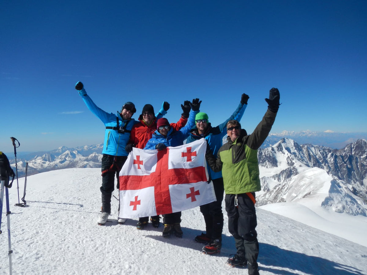 Ghvinos Wine Group founders on summit of Mount Kazbegi (5045m) with snowcapped mountains and high altitude blue skies in background